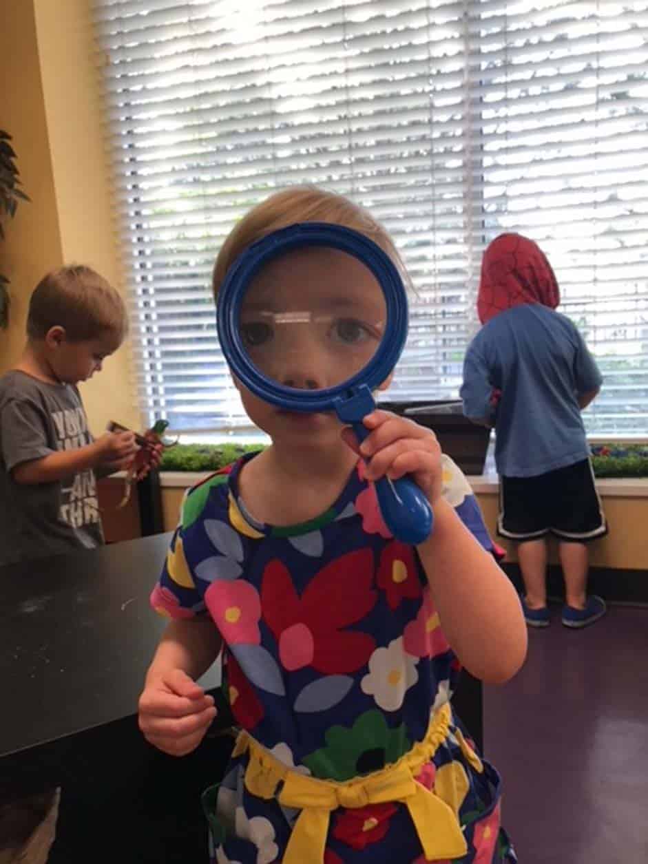 Preschool student exploring with a magnifying glass during a classroom activity.