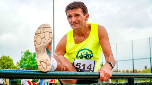 man in yellow tank top stretching before a race